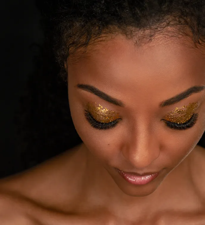Close-up beauty portrait of a woman with gold glitter eyeshadow, long lashes, and defined brows