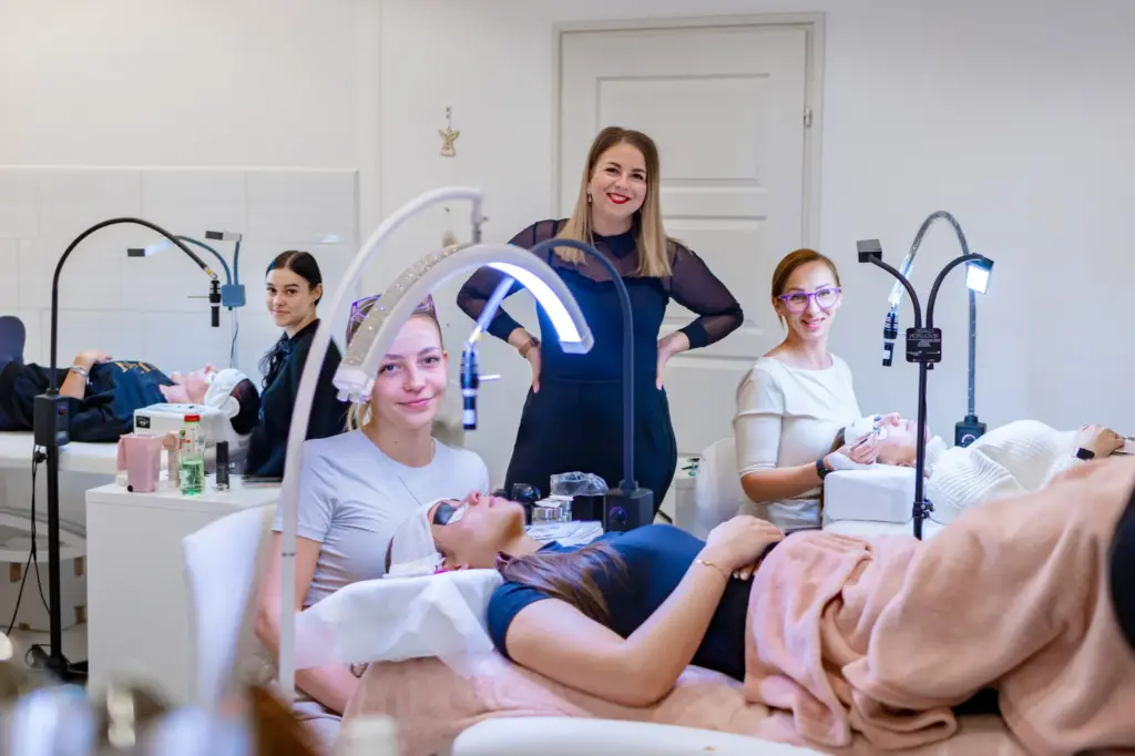 Lash extension students practice on clients as an instructor supervises in a bright training studio