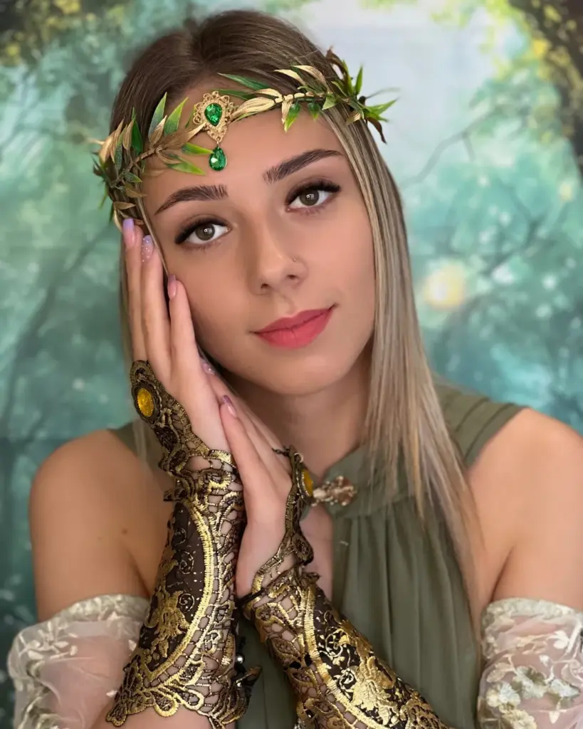 Woman with bold brows and long lashes wearing a jeweled leafy headpiece and ornate gold-and-black gloves