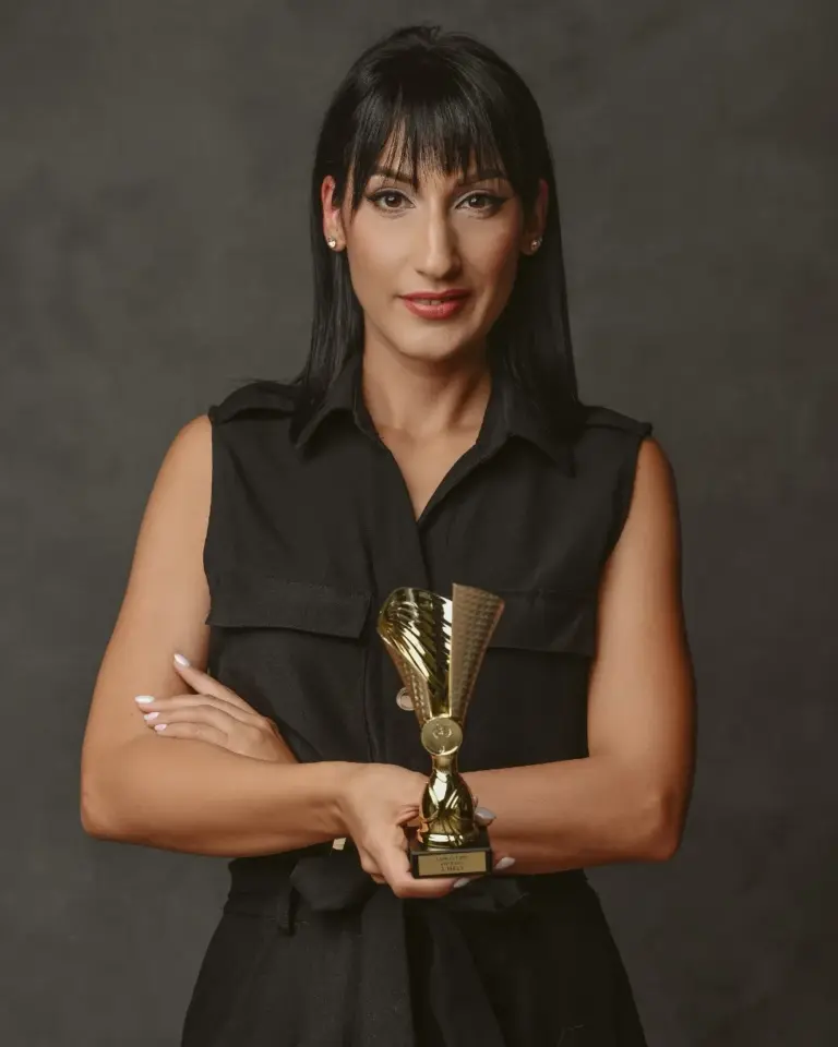 Alexandra Kocsis-Németh poses holding a gold trophy against a dark studio backdrop.