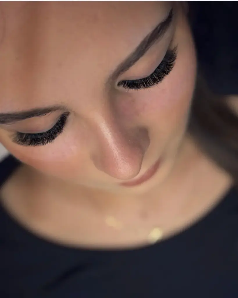 Close-up of a woman with her eyes closed, showing long, dense eyelash extensions and shaped brows.