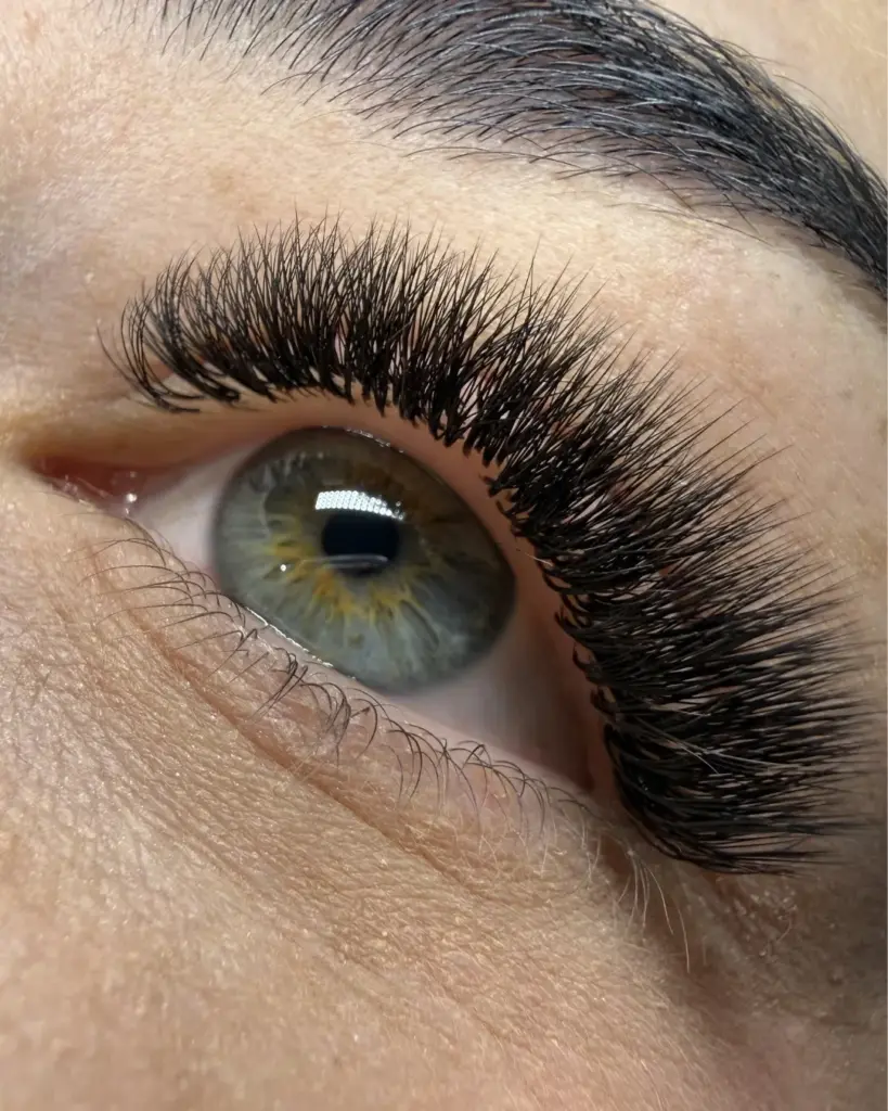 Close-up of a hazel-green eye with dense, long black lash extensions and a dark groomed eyebrow