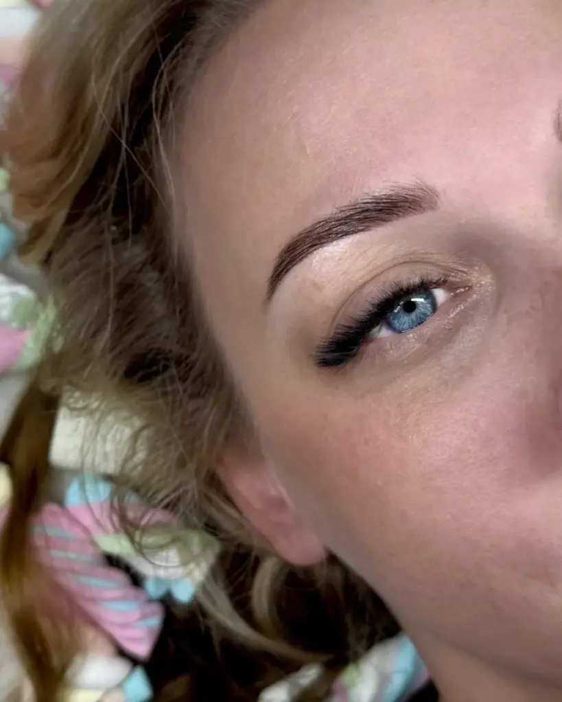 Close-up of a blue eye with long black lash extensions, a shaped dark eyebrow, and neutral eyeshadow.