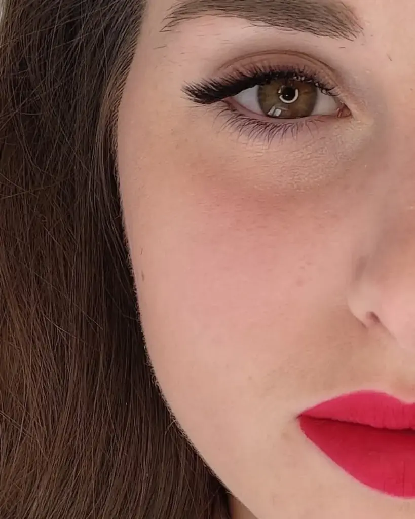 Close-up of a woman with long curled lash extensions, a defined brow, and bright red lipstick.