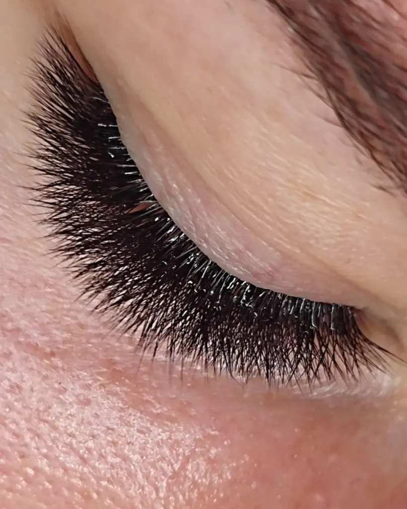 Close-up of a closed eye with dense black lash extensions as a finger gently holds the eyelid.