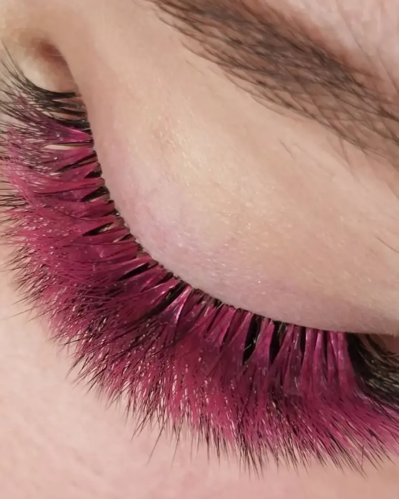 Close-up of a closed eye with long, vivid magenta eyelash extensions.