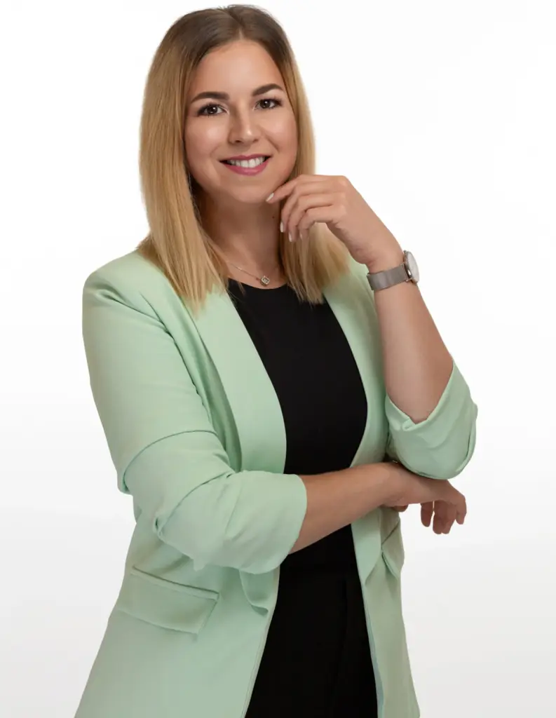 Smiling woman with long blonde hair poses in a mint blazer and black top against a white background.