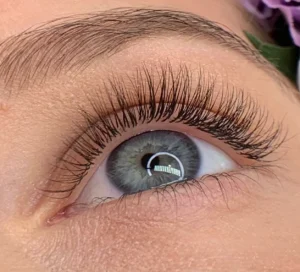Close-up of a gray-blue eye with long, curled lash extensions and a shaped eyebrow.