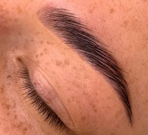 Close-up of a closed eye with long lashes, a full dark eyebrow, and freckled skin