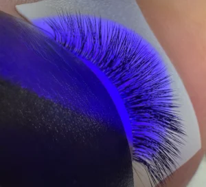 Closed eye with eyelash extensions being cured under a purple UV light, protected by under-eye pads.