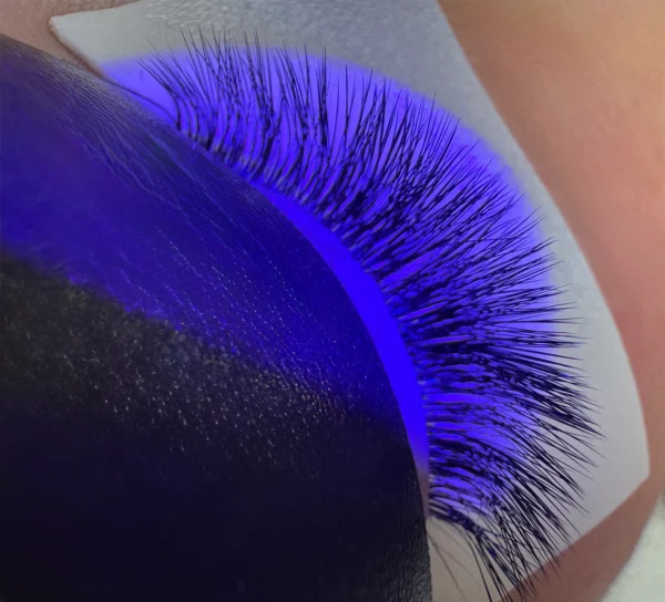 Closed eye with eyelash extensions being cured under a purple UV light, protected by under-eye pads.