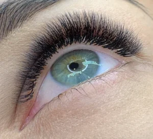 Close-up of a green eye with long, voluminous black lash extensions and a shaped eyebrow