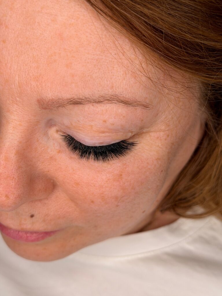 Close-up of a woman with her eye closed, showing full black lash extensions and a natural brow.