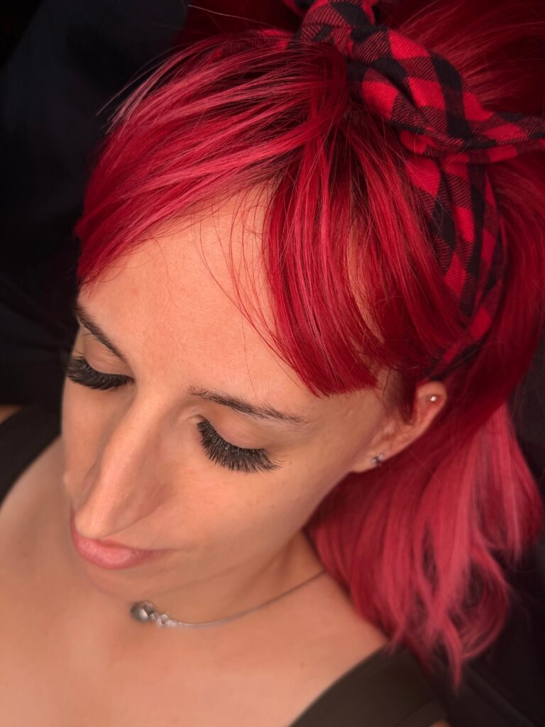 Close-up of a red-haired woman with her eyes closed, showcasing long, full eyelash extensions.