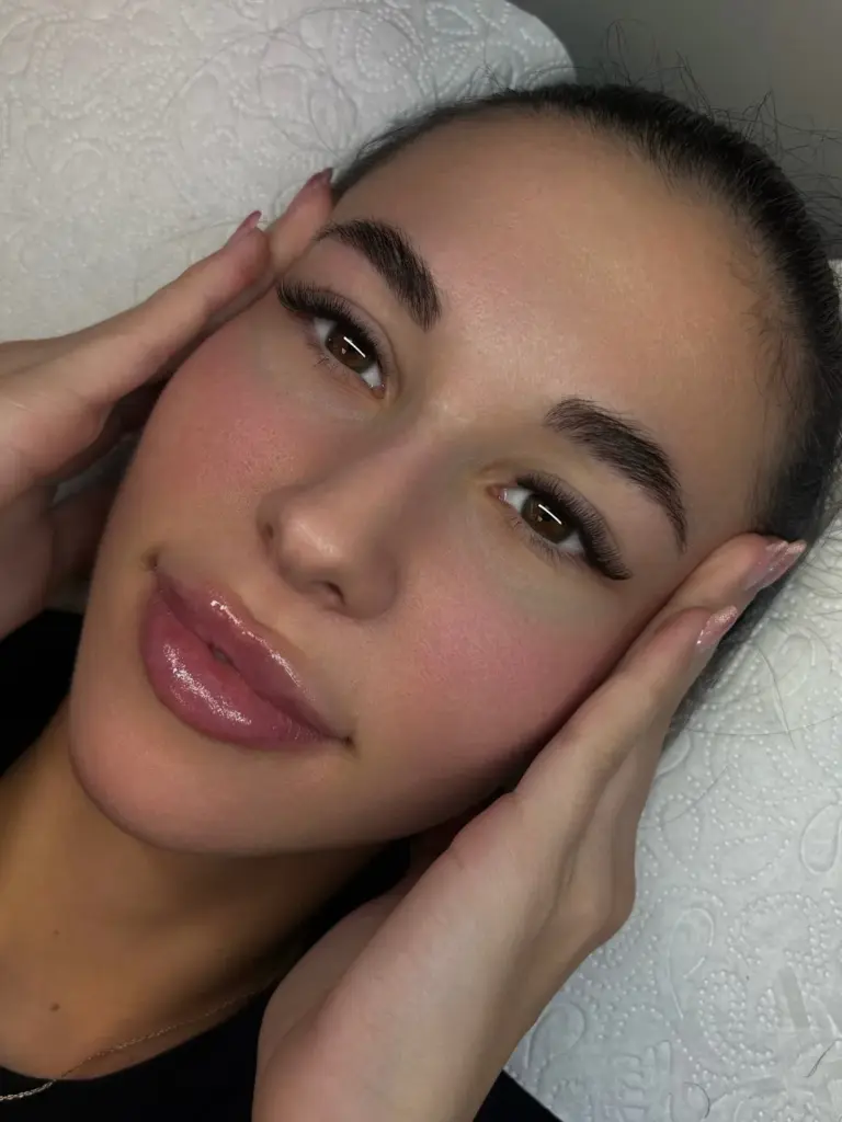 Close-up of a woman with long lash extensions and shaped brows, lying on a treatment bed.