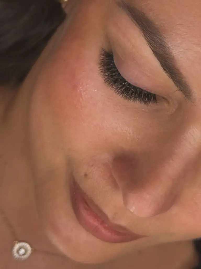 Close-up of a woman with her eye closed, showing full dark lash extensions and a shaped eyebrow.