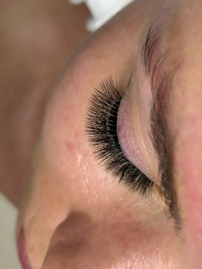 Close-up of a closed eye with long, dense black lash extensions and a natural eyebrow.