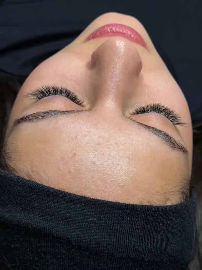 Close-up of a client with eyes closed, showing full black lash extensions and natural shaped brows.