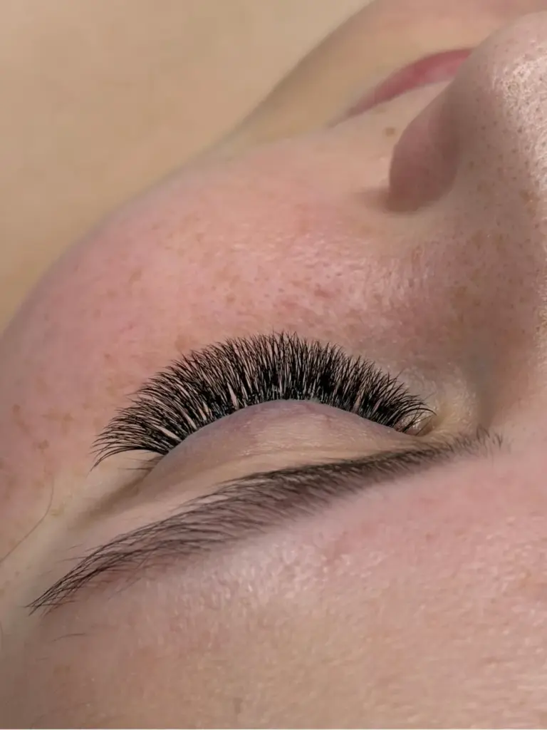 Close-up of a closed eye with dense, curled black lash extensions and a natural eyebrow.