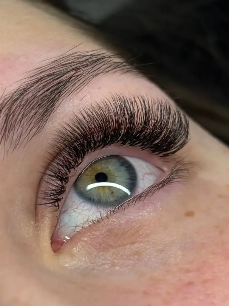 Close-up of a green-hazel eye with dense, curled lash extensions and a natural, shaped eyebrow