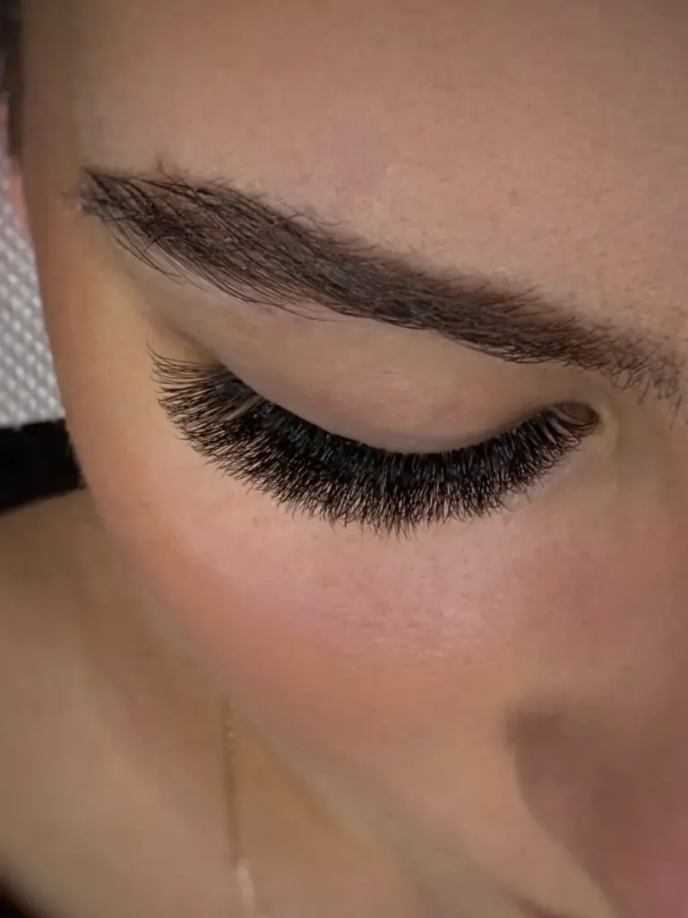 Close-up of a closed eye with dense, curled lash extensions and a neatly shaped dark eyebrow.