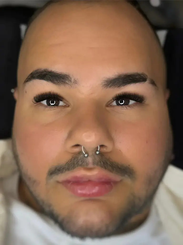 Close-up of a person with long, voluminous eyelash extensions, shaped dark brows and a septum ring.