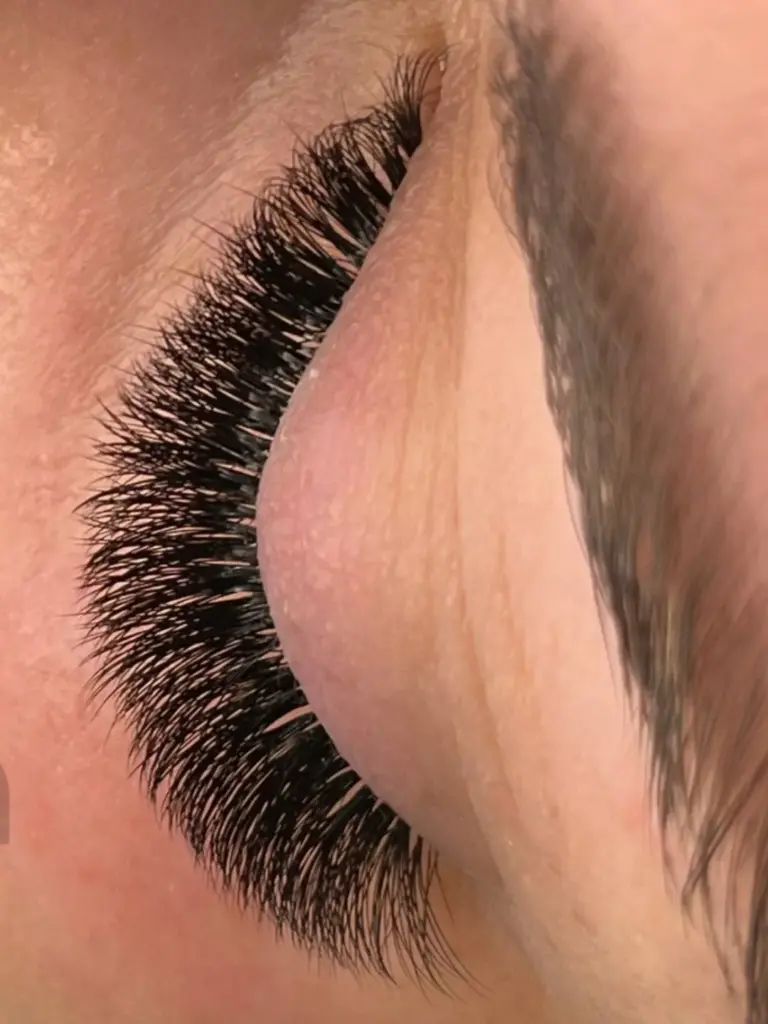 Close-up of a closed eye with dense, dark eyelash extensions and a shaped eyebrow.