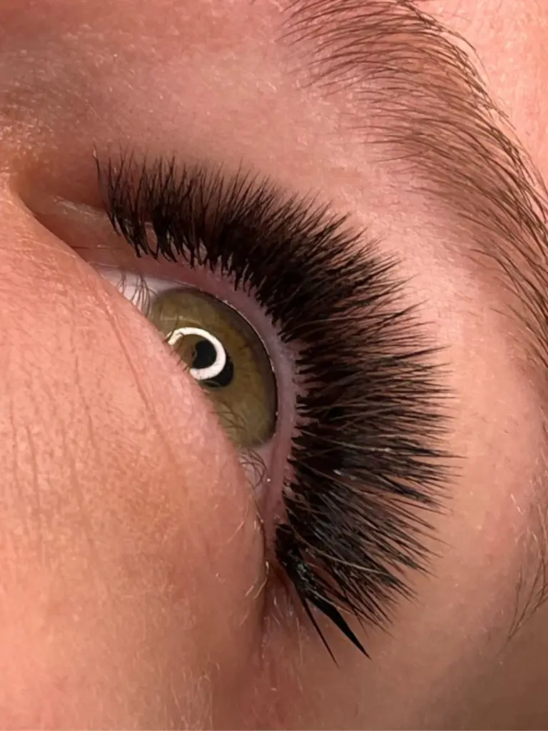 Close-up of a hazel eye with long, dark eyelash extensions and a neatly shaped eyebrow