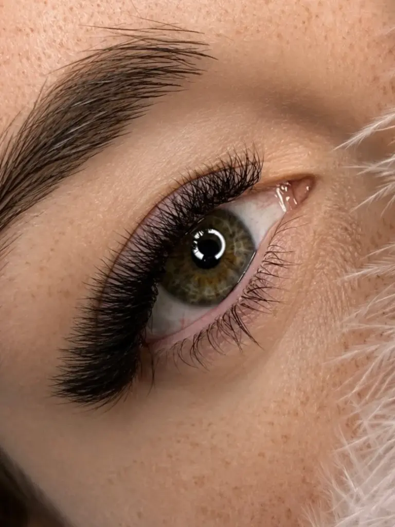 Close-up of a hazel-green eye with voluminous black lash extensions and a neatly shaped eyebrow