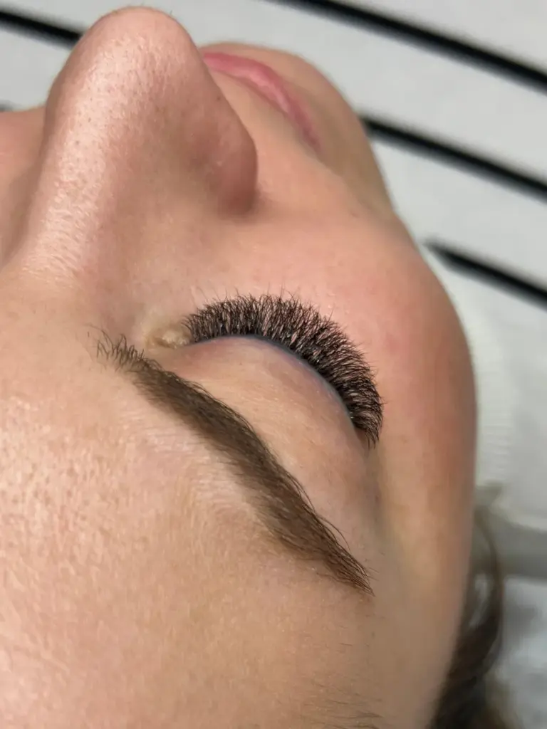 Close-up of a woman with dense eyelash extensions and a neatly shaped eyebrow, lying with her eye closed.