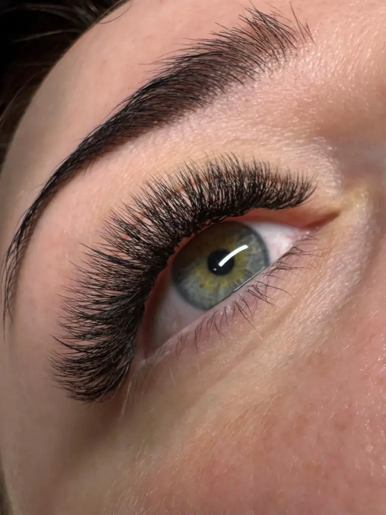 Close-up of a green eye with dramatic black lash extensions and a neatly shaped dark eyebrow.