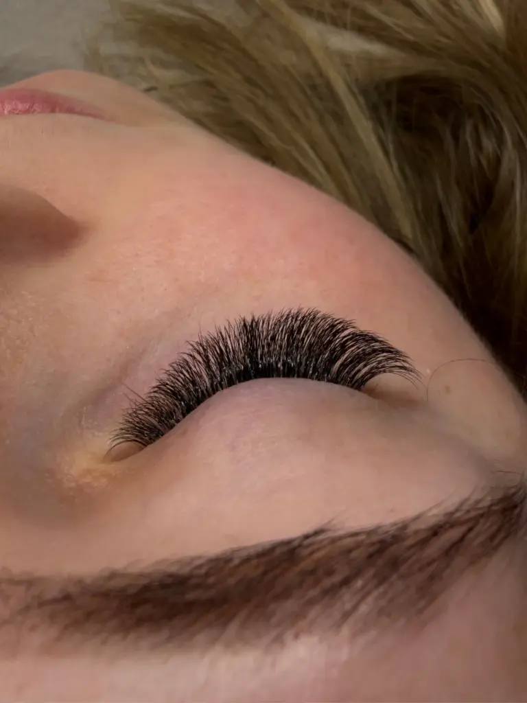 Close-up of a closed eye with dense, curled black lash extensions and a natural brown eyebrow.
