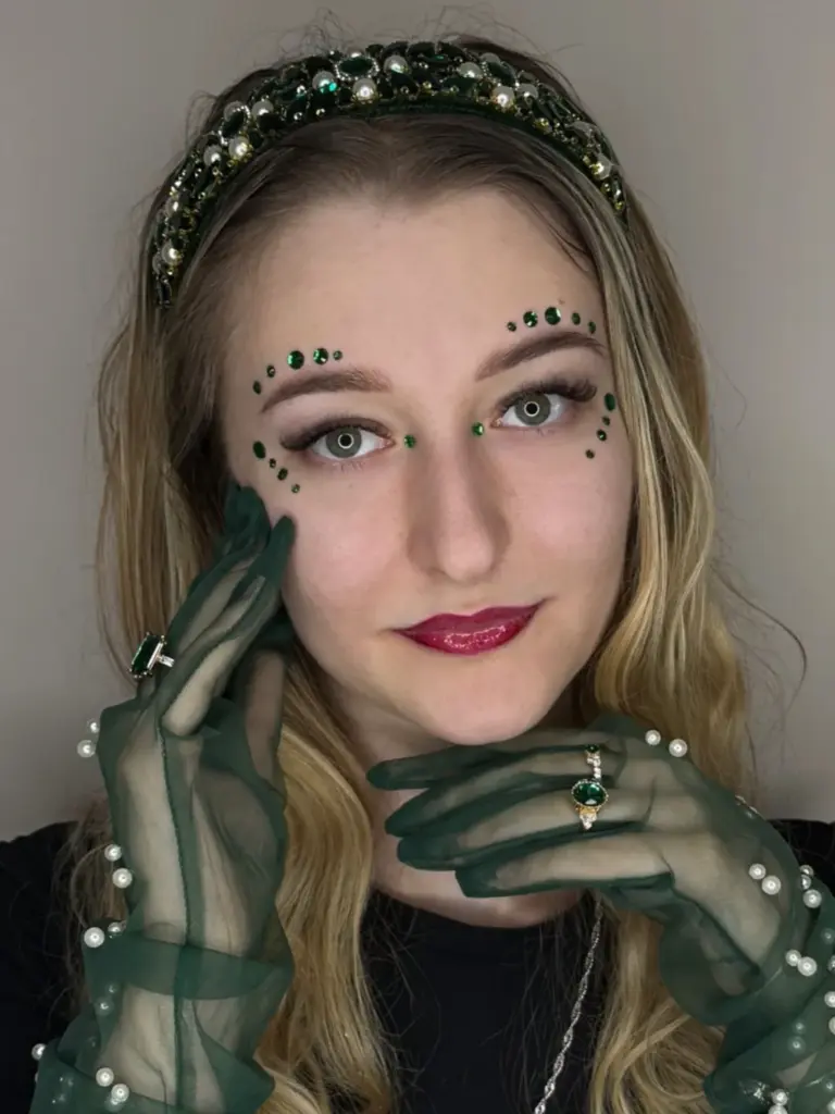 Woman with long lashes, green facial gems, a jeweled headband, and sheer green gloves