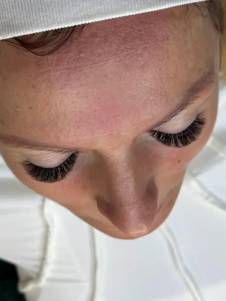 Close-up of a client with eyes closed, showing dense, curled lash extensions beneath a white headband.