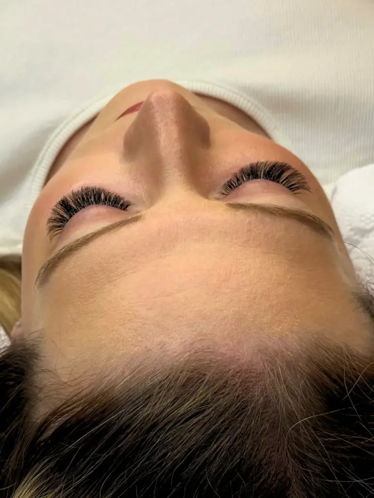 Close-up of a client with long, voluminous eyelash extensions and neatly shaped brows, lying with eyes closed.