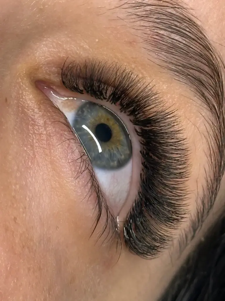 Close-up of a green-gray eye with long, dense black lash extensions and a neatly shaped eyebrow.