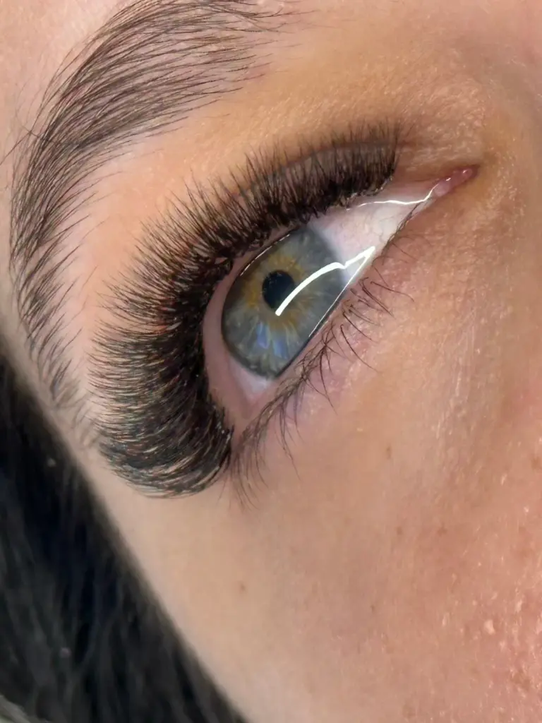 Close-up of a blue-gray eye with long, voluminous lash extensions and a shaped eyebrow
