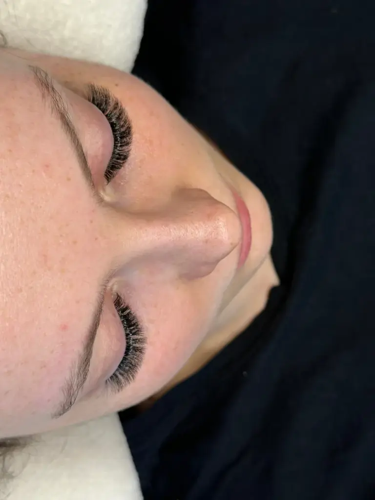 Close-up of a client with eyes closed and full, curled black lash extensions during a beauty treatment