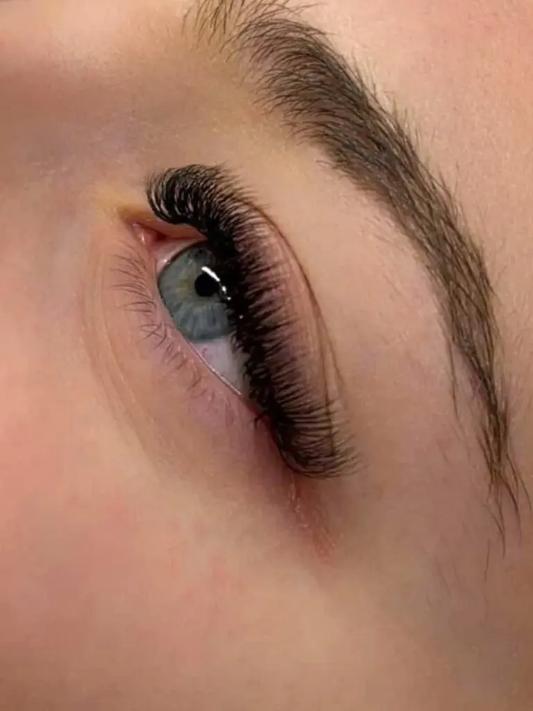 Close-up of a blue-gray eye with long, voluminous black lash extensions and a natural dark eyebrow.