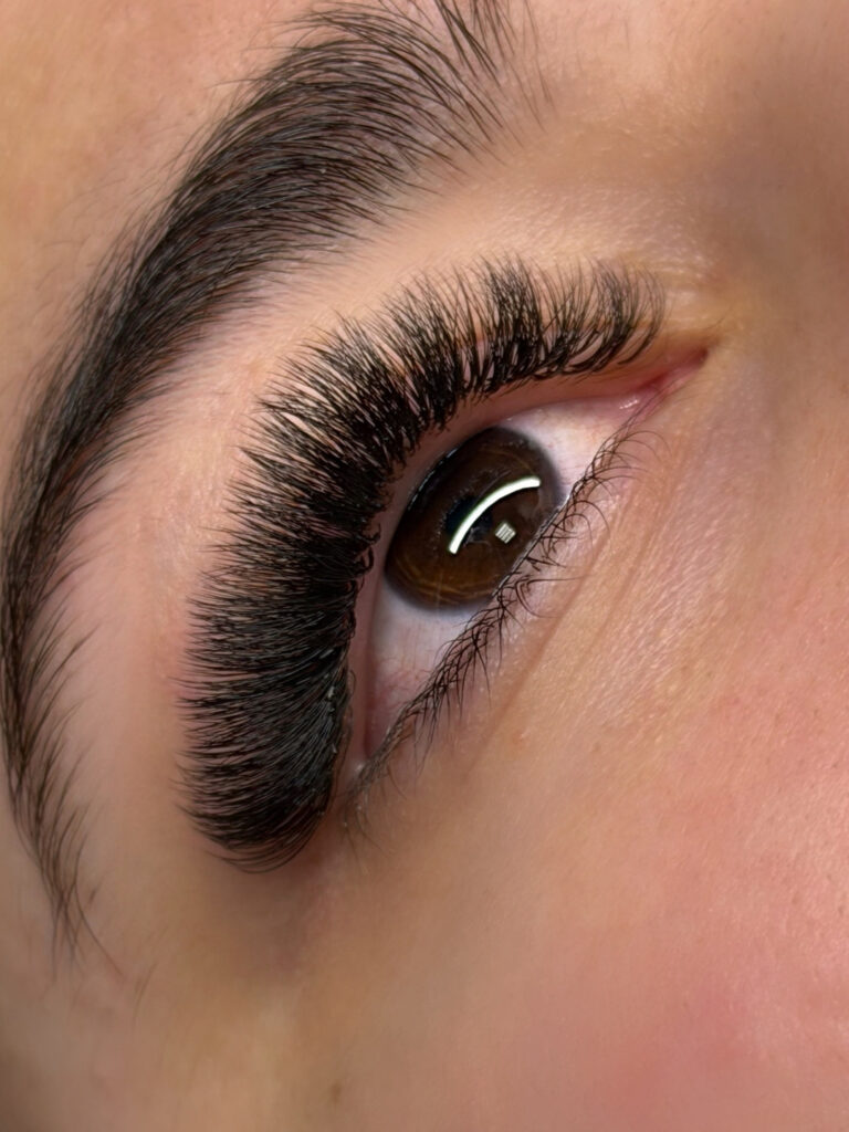 Close-up of a brown eye with dense, curled black lash extensions and a neatly shaped eyebrow.