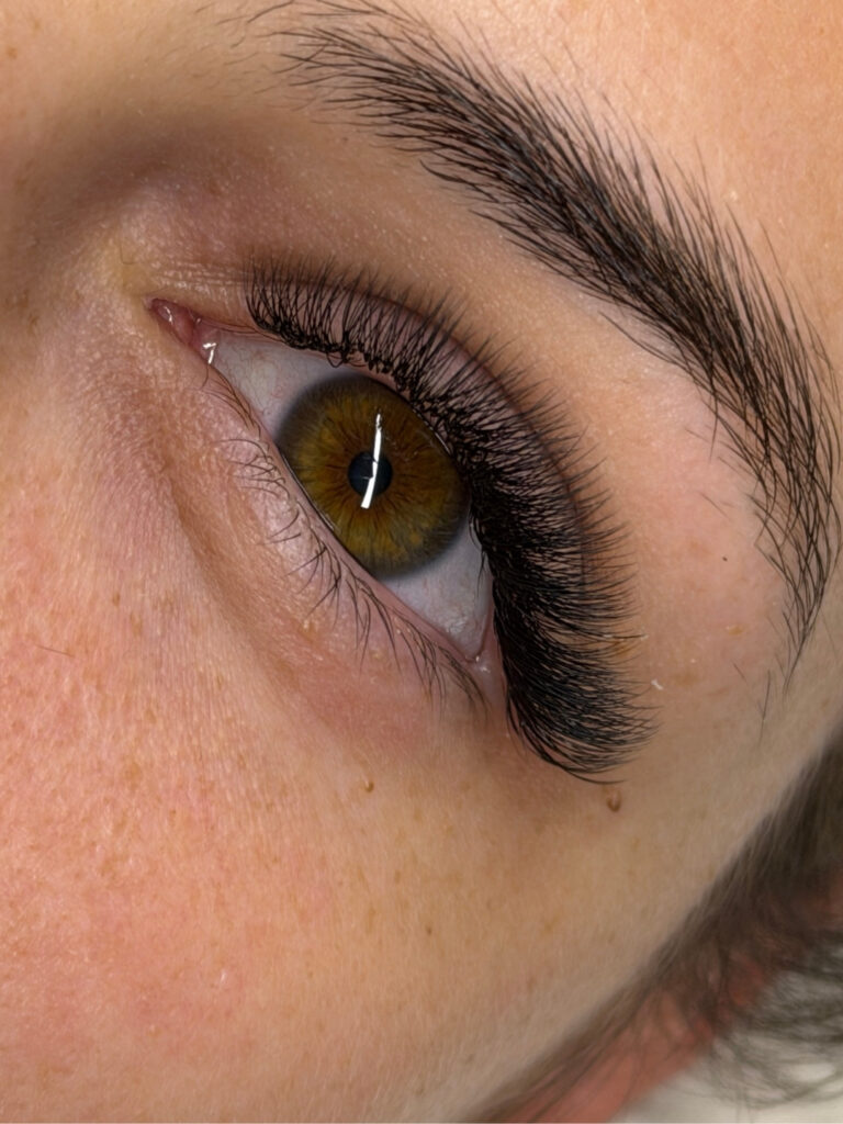 Close-up of a hazel eye with long, voluminous eyelash extensions and a shaped dark eyebrow.