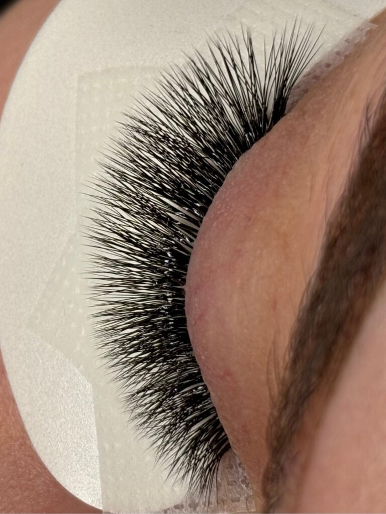 Close-up of a closed eye with dense, long black lash extensions and an under-eye pad.