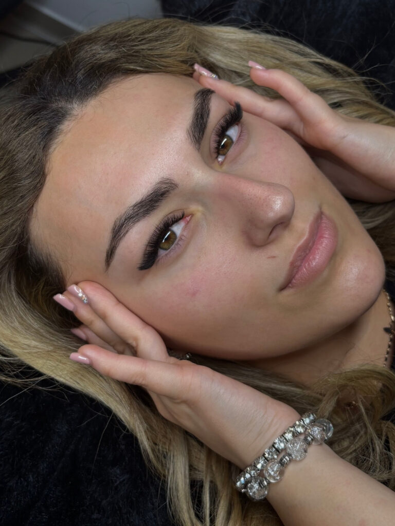 Close-up of a woman showcasing sculpted brows and voluminous lash extensions, with hands framing her face