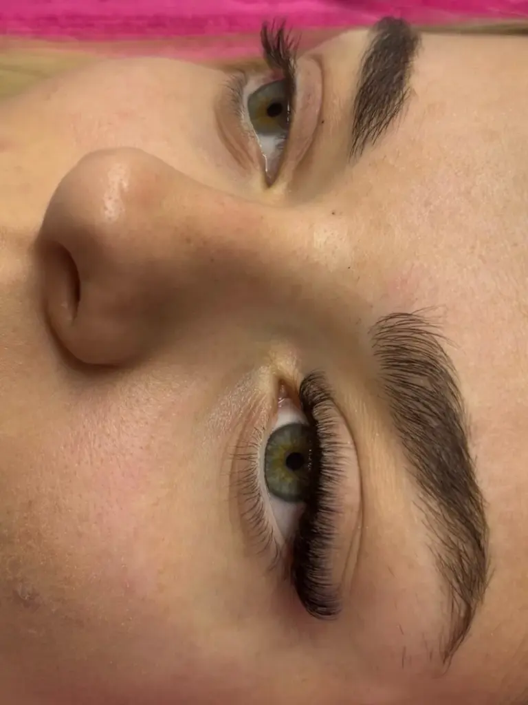 Close-up of green eyes with long, curled lash extensions and neatly shaped dark brows