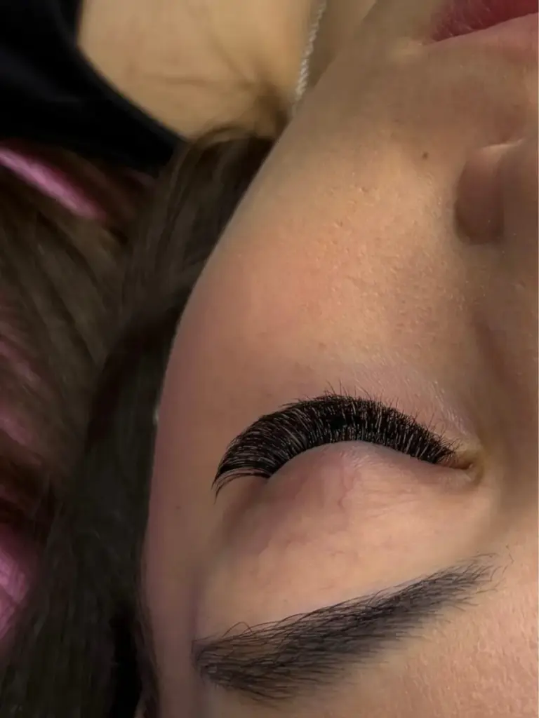 Close-up of a closed eye with dense curled lash extensions and a neatly shaped eyebrow.