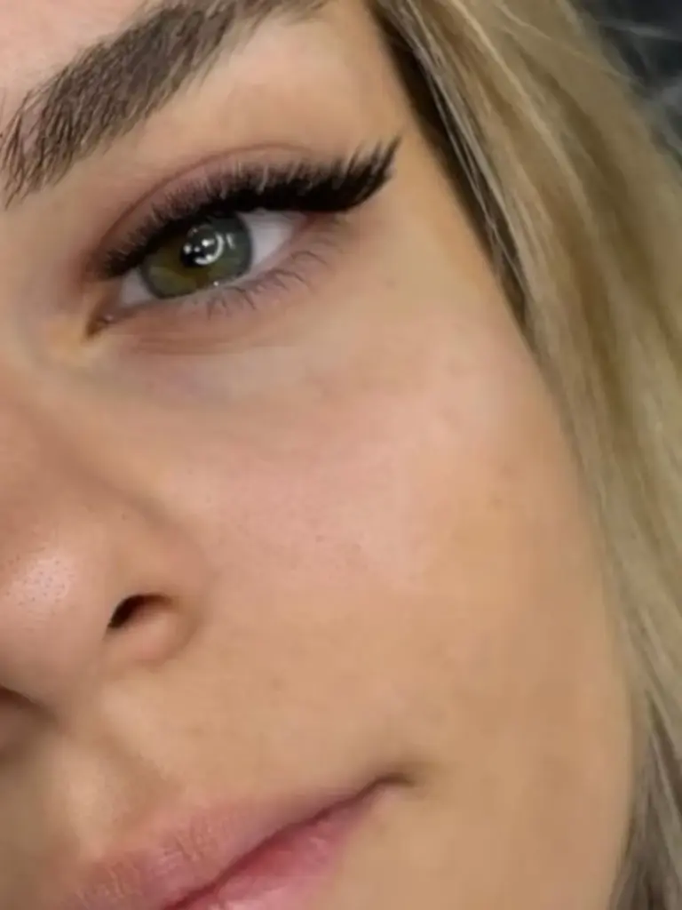 Close-up of a green eye with long, dramatic eyelash extensions and a defined eyebrow.