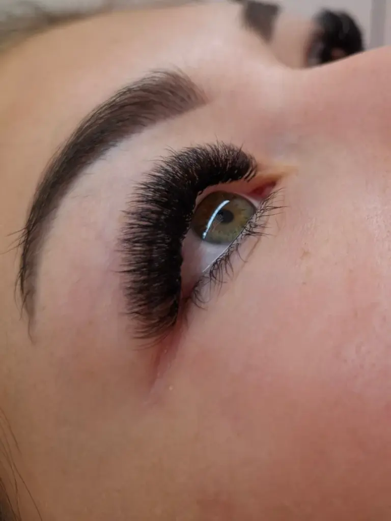 Close-up of a green eye with dense, curled black eyelash extensions and a neatly shaped brow.