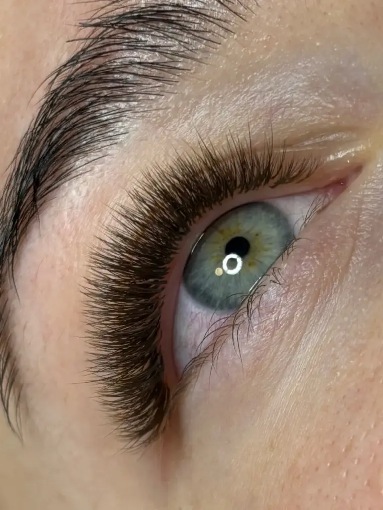Close-up of a blue-green eye with long, dense lash extensions and a neatly shaped dark eyebrow.