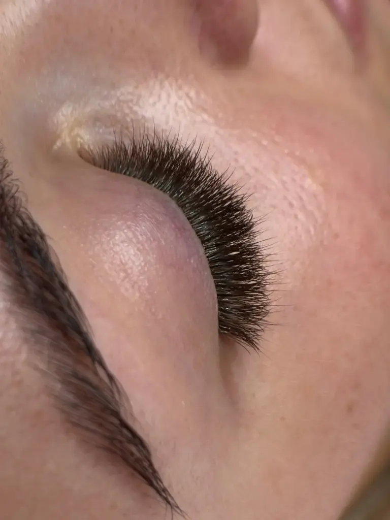 Close-up of a closed eye with dense, long black eyelash extensions and a shaped eyebrow
