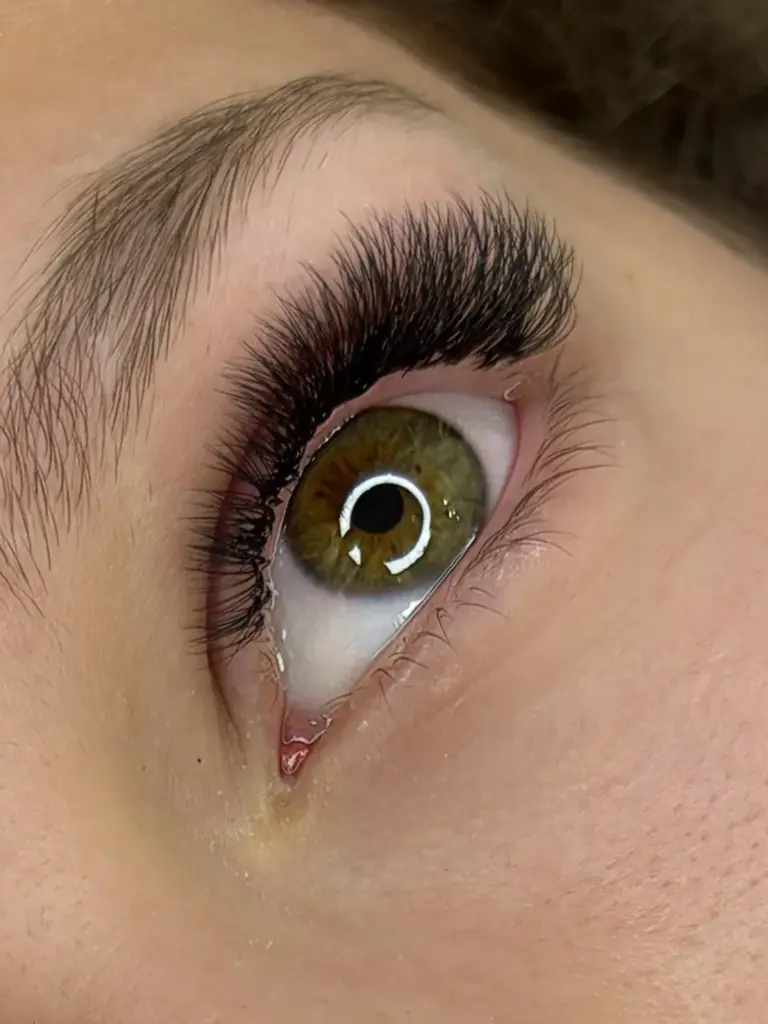 Close-up of a green-hazel eye with dense, curled lash extensions and a neatly shaped eyebrow